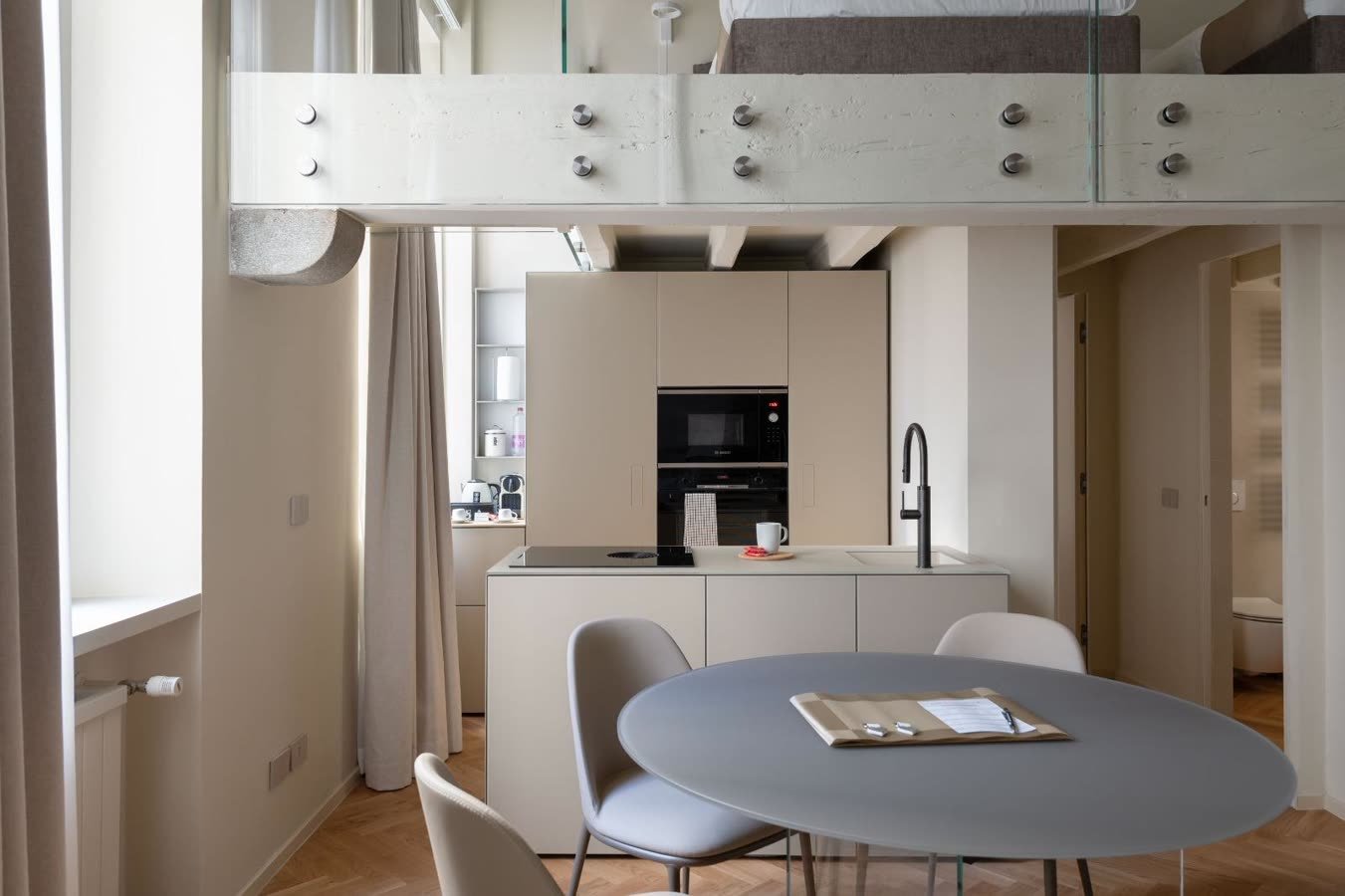 Cucina in linea e tavolo tondo accanto alla vetrata del soppalco