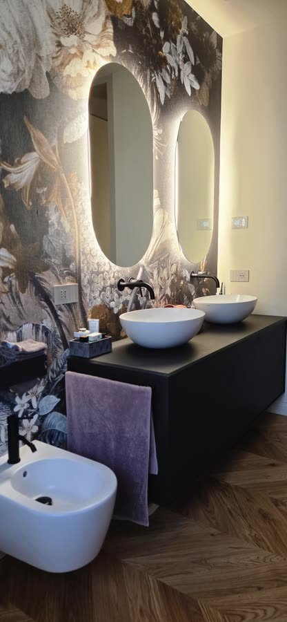 Bagno con parete decorata a fiori e specchio ovale retroilluminato