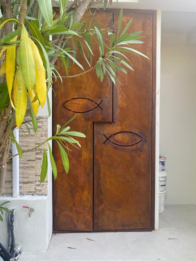Porta in acciaio corten con pesci intagliati, accanto a un oleandro
